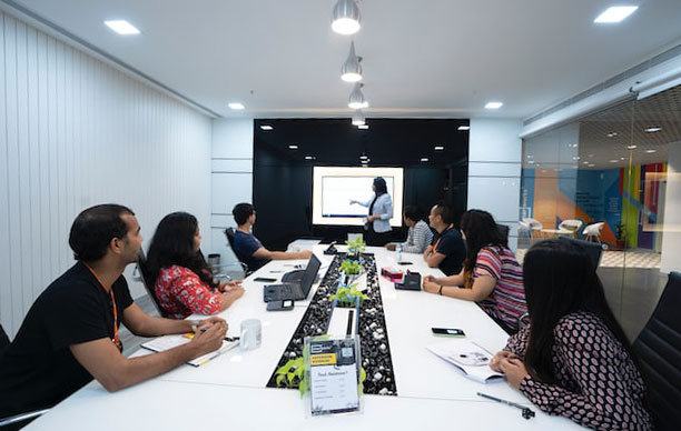 An office board room where a woman is presenting a PowerPoint presentation.