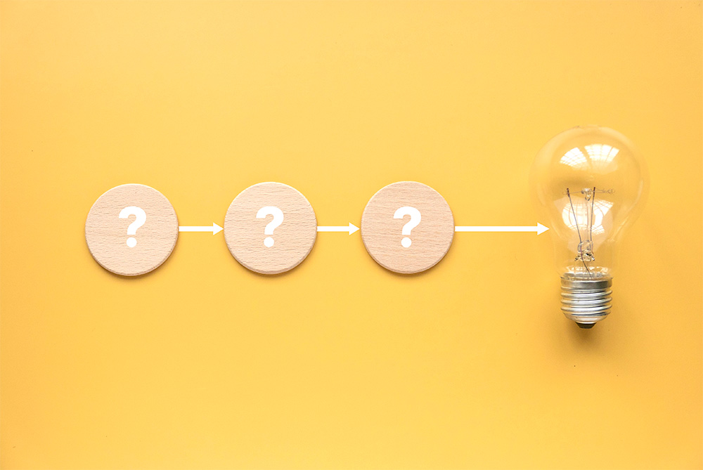 Three question marks and a light bulb with arrows between them representing the process of getting an idea.